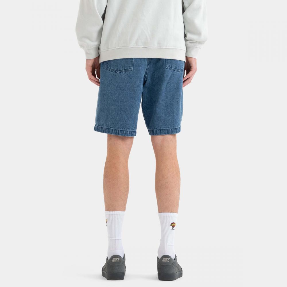 A person shown from the back wearing medium-wash blue denim shorts, a light gray sweatshirt, white socks, and dark gray slip-on shoes against a plain light gray studio background.
